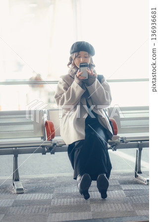 A woman in winter sitting at a bus stop and looking at her smartphone A woman in winter sitting at a bus stop and looking at her smartphone 136936681