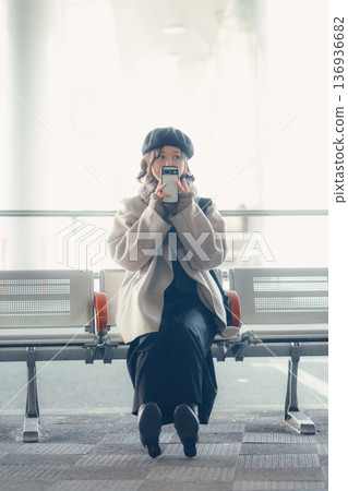 A woman in winter sitting at a bus stop and looking at her smartphone A woman in winter sitting at a bus stop and looking at her smartphone 136936682