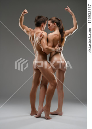 Muscular man and graceful woman in an artistic nude embrace against a gray background. 136938387