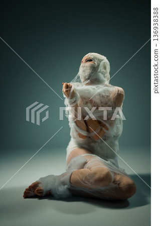Bound figure wrapped in white fibrous material struggles for freedom on a gray background. Bound figure wrapped in white fibrous material struggles for freedom on a gray background. 136938388