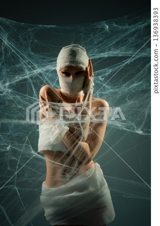 Mysterious woman in mummy costume with dramatic makeup surrounded by cobwebs 136938393