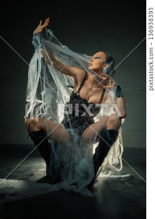 Gothic woman in a black corset and boots posing dramatically, caught in a giant spiderweb. 136938395