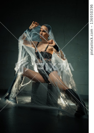 Powerful woman in black lingerie and boots trapped in a giant spiderweb against a dark background. Powerful woman in black lingerie and boots trapped in a giant spiderweb against a dark background. 136938396