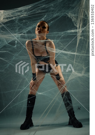 Powerful woman in a black leather outfit and boots, entangled in a large spiderweb. 136938402