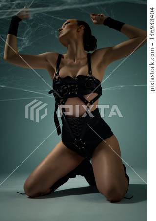 Powerful woman in a black leather harness kneeling under spiderwebs in a dramatic pose Powerful woman in a black leather harness kneeling under spiderwebs in a dramatic pose 136938404