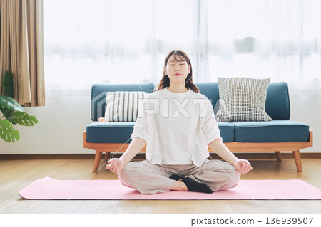一位30多歲的女性在家中進行冥想和深呼吸，實踐正念生活方式。 136939507