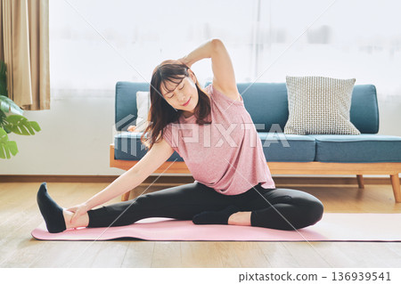 一位30多歲的女性在客廳做瑜伽,展現她的健身生活 一位30多歲的女性在客廳做瑜伽,展現她的健身生活 136939541