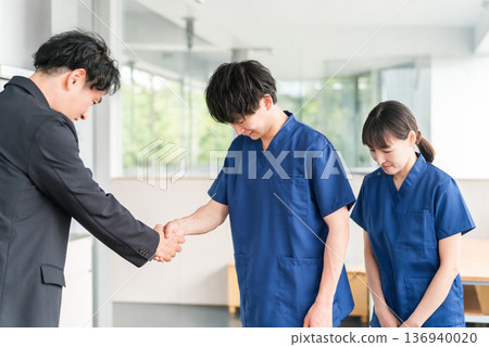 一位來自醫療設備製造商的商人和一位身穿手術服的醫生握手 一位來自醫療設備製造商的商人和一位身穿手術服的醫生握手 136940020