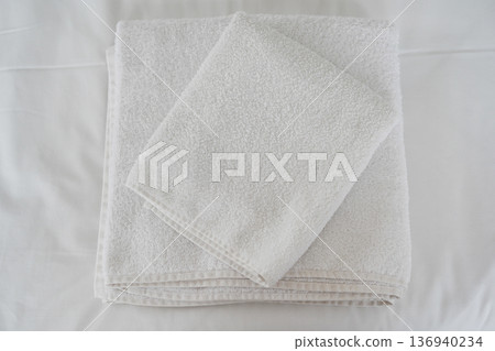 Folded white cotton towels on clean minimalist bed linen background Folded white cotton towels on clean minimalist bed linen background 136940234