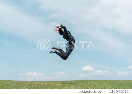 A young businessman in a suit jumping up on a hill 136941011