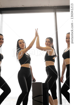 A group of women in athletic wear celebrate their fitness achievement with a high five, embodying teamwork and success 136941213