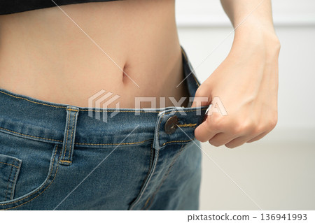 Young Asian woman losing weight wearing loose pants in oversize jeans. 136941993