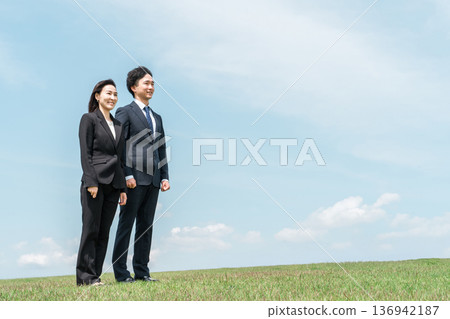 A businessman and a businesswoman in suits standing on a hill under a blue sky (challenge, challenge, spirit of challenge) A businessman and a businesswoman in suits standing on a hill under a blue sky (challenge, challenge, spirit of challenge) 136942187