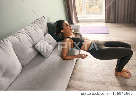 Fitness enthusiast performing tricep dips in a modern living room with natural light and minimalistic decor during a home workout session Fitness enthusiast performing tricep dips in a modern living room with natural light and minimalistic decor during a home workout session 136942602