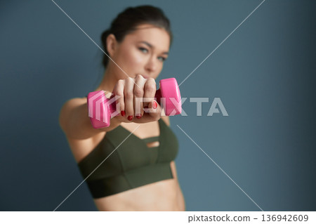 Woman exercising with pink dumbbell in a fitness studio focused on strength training and wellness during daytime Woman exercising with pink dumbbell in a fitness studio focused on strength training and wellness during daytime 136942609