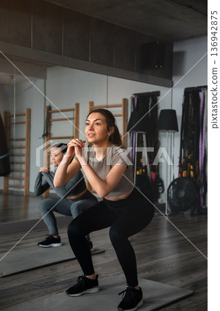 Woman trains in a gym while another person exercises in the background during a fitness session in the afternoon Woman trains in a gym while another person exercises in the background during a fitness session in the afternoon 136942875