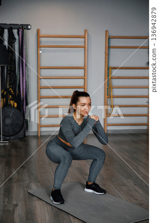 Woman performs squats in gym during training session at indoor fitness center 136942879