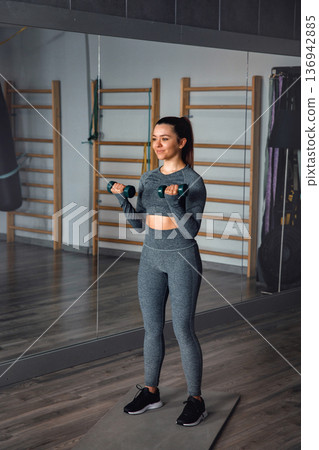 Woman exercises with dumbbells while training in a gym in the morning Woman exercises with dumbbells while training in a gym in the morning 136942885
