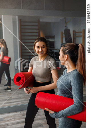 Women prepare for yoga class with mats in gym during afternoon training session in fitness center Women prepare for yoga class with mats in gym during afternoon training session in fitness center 136942889