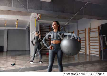 Woman shows strength while holding a fitness ball in a gym during workout session Woman shows strength while holding a fitness ball in a gym during workout session 136942894