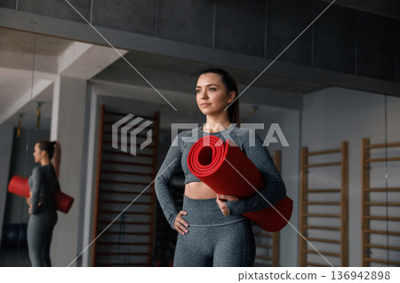 Woman holding a red yoga mat in a gym during her fitness training session in the morning light 136942898