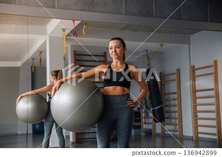 Woman in gym holding a fitness ball and preparing for her workout routine with focus on health and fitness Woman in gym holding a fitness ball and preparing for her workout routine with focus on health and fitness 136942899