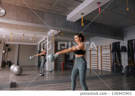 Woman training with kettlebell in modern gym space during afternoon Woman training with kettlebell in modern gym space during afternoon 136942901
