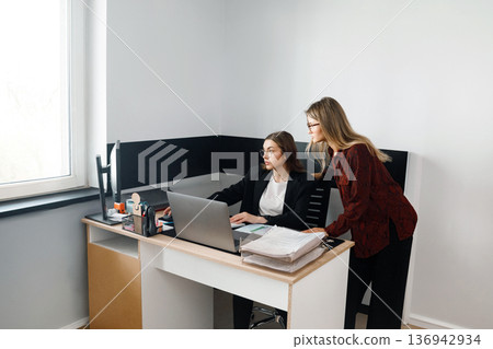 Business women work together at desk in office environment during the day 136942934