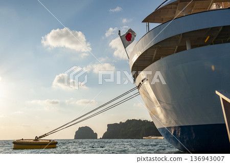 一艘豪華遊輪停泊在父島港的浮標旁，沐浴在夕陽和日本國旗的餘暉中。 136943007