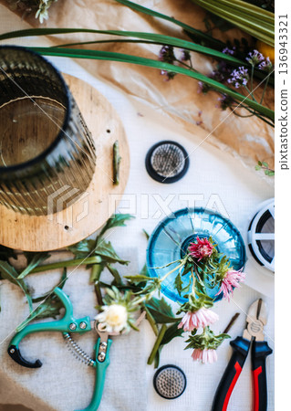 Overhead view shows smartphone on table surrounded by florist tools and botanical stems for flower arranging. Floral masterclass, botanical education, creative flower arranging course. Overhead view shows smartphone on table surrounded by florist tools and botanical stems for flower arranging. Floral masterclass, botanical education, creative flower arranging course. 136943321