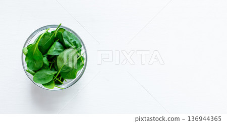 Fresh green spinach leaves in glass bowl on white table. Fresh green spinach leaves in glass bowl on white table. 136944365
