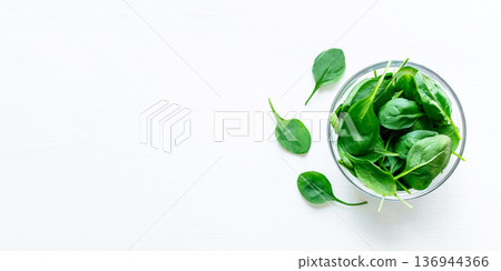 Fresh green spinach leaves in glass bowl on white table. Fresh green spinach leaves in glass bowl on white table. 136944366
