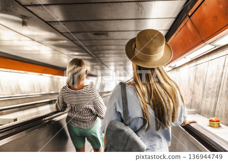 Two women descending escalator in metro tunnel, urban travel and public transportation concept Two women descending escalator in metro tunnel, urban travel and public transportation concept 136944749