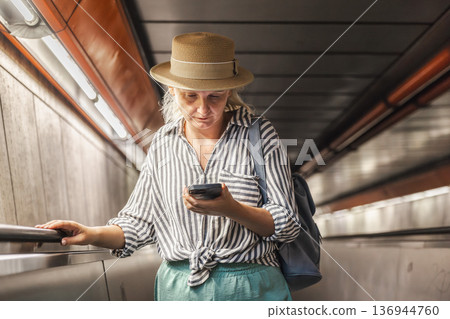 Woman using smartphone while descending escalator in subway tunnel during urban commute Woman using smartphone while descending escalator in subway tunnel during urban commute 136944760