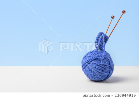 Blue knitted wool on gray blue background with knitting needles for knitting warm clothes and hobbies needlework Blue knitted wool on gray blue background with knitting needles for knitting warm clothes and hobbies needlework 136944919
