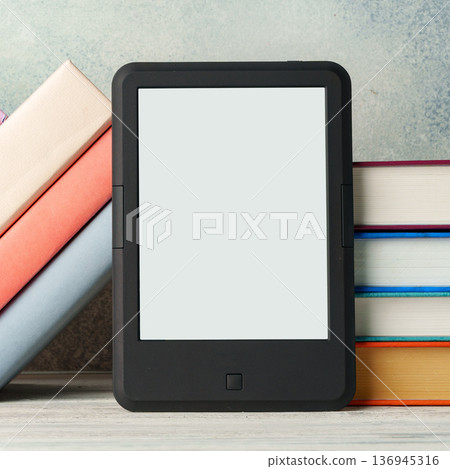 E-reader resting between stacks of colorful books on a table in a cozy reading space 136945316
