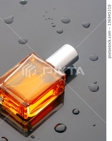 Bottle of orange liquid on dark surface with water droplets around it 136945319