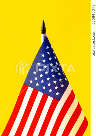 Flag of the United States placed on a yellow background with a black crayon on top 136945378