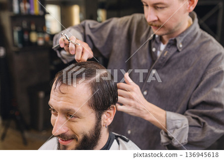 Barber cutting male client hair with scissors and comb. Close up of professional haircut process, precision technique, men grooming service in modern barbershop. Barber cutting male client hair with scissors and comb. Close up of professional haircut process, precision technique, men grooming service in modern barbershop. 136945618