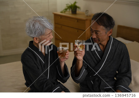 Senior couple sitting on the bed in a gown coat Lifestyle image Senior couple sitting on the bed in a gown coat Lifestyle image 136945716