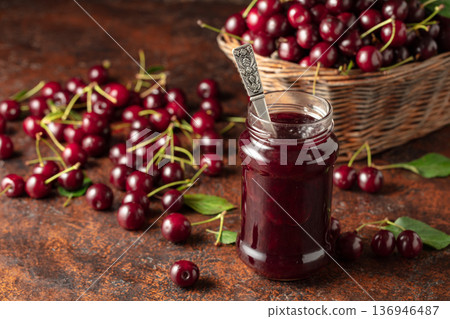 Cherry jam and fresh berries with leaves on an old brown table. Cherry jam and fresh berries with leaves on an old brown table. 136946487