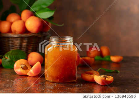 Apricot jam in glass jar and fresh fruits on a brown table. Apricot jam in glass jar and fresh fruits on a brown table. 136946590