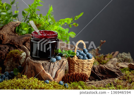 A jar of blueberry jam with fresh berries on an old tree trunk in the forest. A jar of blueberry jam with fresh berries on an old tree trunk in the forest. 136946594