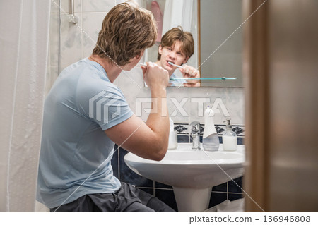 Man brushing teeth sitting near bathroom sink Man brushing teeth sitting near bathroom sink 136946808