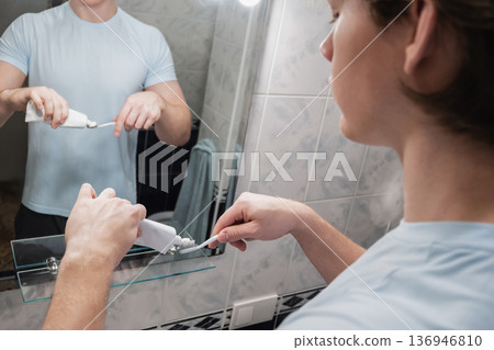 Man applying toothpaste on toothbrush in bathroom mirror 136946810