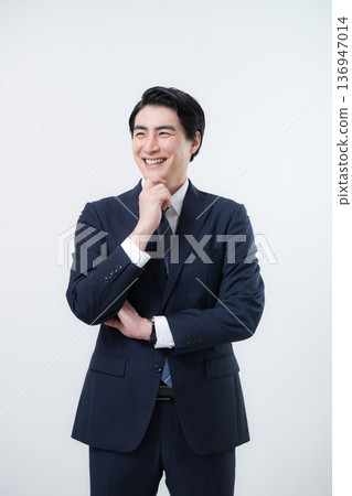一位英俊的中年商務人士站著，上半身，面帶微笑，似乎在思考，又有些憂慮，一手托著下巴，抬頭望向天空。 136947014