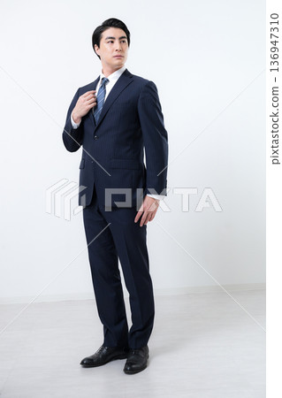 Smiling male businessman in a suit adjusting his collar. 136947310