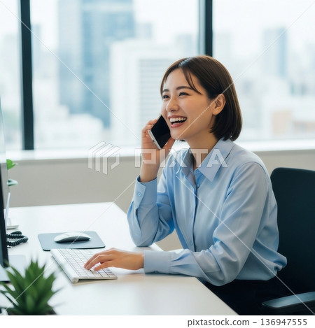 一位年輕的女員工在辦公室裡面帶著微笑地用智慧型手機通話。 136947555