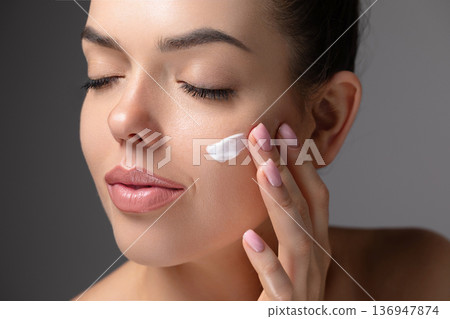 Skin care. Beauty close up portrait of young woman with a glowing skin is applying a skincare product. Hydration. Cream smear. Beautiful model with natural makeup touching her skin. 136947874