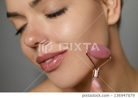 Beautiful woman, her eyes closed and massaging face roller. Face massage. Beautiful woman, her eyes closed and massaging face roller. Face massage. 136947879